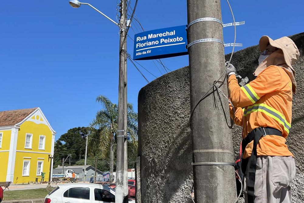 A placa possui cor azul, nome completo (ex: Marechal Floriano Peixoto) e o bairro (ex: Alto da XV). 