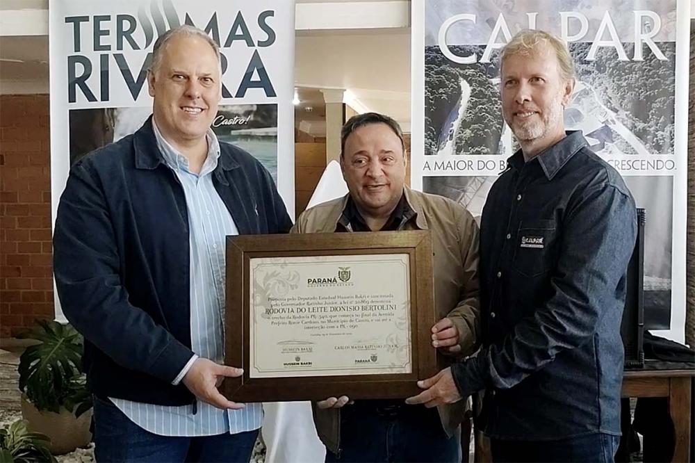 Os irmãos Paulo e Marcus Bertolini recebem das mãos do deputado estadual Hussein Bakri a lei que denomina o trecho da Rodovia PR-340, Rodovia do Leite, Dionisio Bertolini. Foto Toninho Anhaia